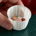 A hand holding a Genpak paper souffle cup with pills in it.