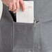 A person putting a receipt in the pocket of an Acopa Kennett gray denim half bistro apron.