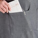 A person's hand putting a piece of paper in a pocket on an Acopa Kennett gray denim restaurant apron.