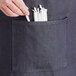 A person's hand holding a pair of white straws in an Acopa Kennett blue denim bistro apron pocket.