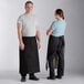 A man and woman wearing Acopa black bistro aprons over black pants.
