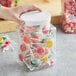 A hand holding a 64 oz. square PET plastic jar with white lid filled with candy.