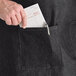 A man wearing an Acopa Kennett black denim bib apron with natural webbing and putting a piece of paper in a pocket.