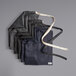 A stack of black denim Acopa Kennett bib aprons with natural webbing straps.