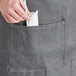 A person putting silverware in the pocket of an Acopa Kennett gray denim bistro apron.