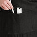 A person putting a pen in the pocket of a black Acopa Kennett bistro apron.