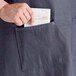 A man putting a piece of paper in the pocket of a blue denim Acopa Kennett bib apron.
