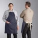 A man and woman wearing blue Acopa Kennett bib aprons with natural webbing.