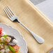 An Acopa Vittoria stainless steel salad fork next to a plate of food.