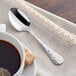 An Acopa Inspira stainless steel teaspoon rests on a napkin next to a cup of coffee.