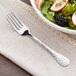 An Acopa Inspira stainless steel salad fork next to a bowl of salad.