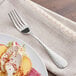 An Acopa stainless steel dinner fork next to a plate of food with a piece of peach on it.