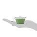 A hand holding a small green floral ramekin with a curved design.