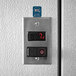 A black rectangular metal panel with a digital thermometer displaying the temperature inside a walk-in cooler.