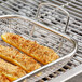 A stainless steel mesh roasting and grill basket of squash on a grill.