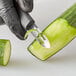 A hand in a black glove using a Mercer Culinary vegetable peeler to peel a cucumber.