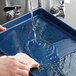 A hand washing a Baker's Mark blue aluminum sheet tray with a sponge.