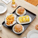 A Baker's Mark black non-stick bun tray on a wood table with a burger, fries, and corn.