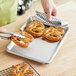 A person using a Baker's Mark stainless steel bun pan to cut pretzels on a plate.