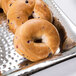 An American Metalcraft hammered stainless steel square tray holding a bagel with blueberries on a counter.