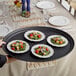 A person holding a black Choice oval non-skid serving tray with four small plates of food.