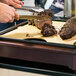 A person cutting meat on a cutting board in a Cal-Mil Westport carving station kit.