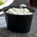 A black oval plastic souffle cup with spinach and cheese in it.
