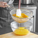 A person stirring egg yolk in a bowl with a Vollrath medium mesh wire strainer with a wood handle.