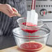 A person using a Vollrath medium mesh wire strainer with a wood handle to pour red liquid into a bowl.