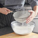 A person sifting flour into a bowl using a Vollrath double mesh strainer with a wood handle.