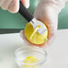 A person in gloves using a Mercer Culinary zester to peel a lemon.