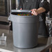 A man in a chef's uniform holding a large gray round ingredient storage bin full of candy.