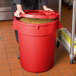 A woman holding a red round ingredient storage bin full of corn.