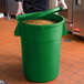 A man holding a green 44 gallon ingredient storage bin with a lid.