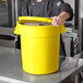 A man in a chef's uniform holding a yellow round ingredient storage bin.