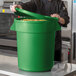 A man in a chef's uniform holding a green round ingredient storage bin.