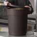 A man in a chef's uniform opening a large brown round storage bin full of candy.
