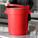 A woman in a black chef's uniform holding a large red round ingredient storage bin.