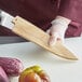 A person in a chef's uniform using a Mercer Culinary Saya Ash Wood Cover to cut vegetables.