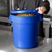 A person holding a blue round ingredient storage bin full of pasta.