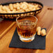 A Libbey Winchester old fashioned glass filled with brown liquid on a wooden tray with peanuts.