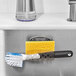 An OXO stainless steel suction sponge holder holding a sponge and brush on the side of a metal sink.