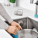 A person washing dishes in a sink with an OXO stainless steel sponge holder.