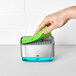 A hand holding a green sponge over a OXO Good Grips Soap Dispensing Sponge Holder.