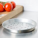 An American Metalcraft tin-plated steel pizza pan with perforations on it next to tomatoes.
