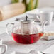 An Acopa Lotus glass teapot with red tea inside on a table.
