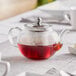 A clear glass Acopa Lotus teapot with red liquid inside on a table.