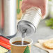 A hand using a stainless steel Tablecraft center pour spout to pour liquid into coffee.