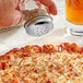 A hand using a Tablecraft stainless steel perforated fluted shaker top to sprinkle pepper on a pizza.
