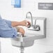 A person washing hands in a Steelton wall mounted hand sink under a gooseneck faucet.